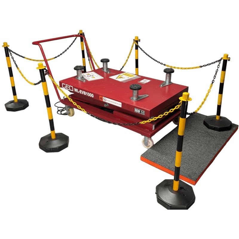 A red hydraulic EV battery lift on a wheeled platform, surrounded by black and yellow safety posts and chains, with a gray floor mat on a white background, front and side view